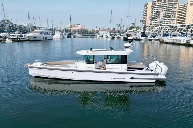 Slide: The Image of 2023 Axopar 28 Cabin boat docked in a marina with yachts in the background. - 5