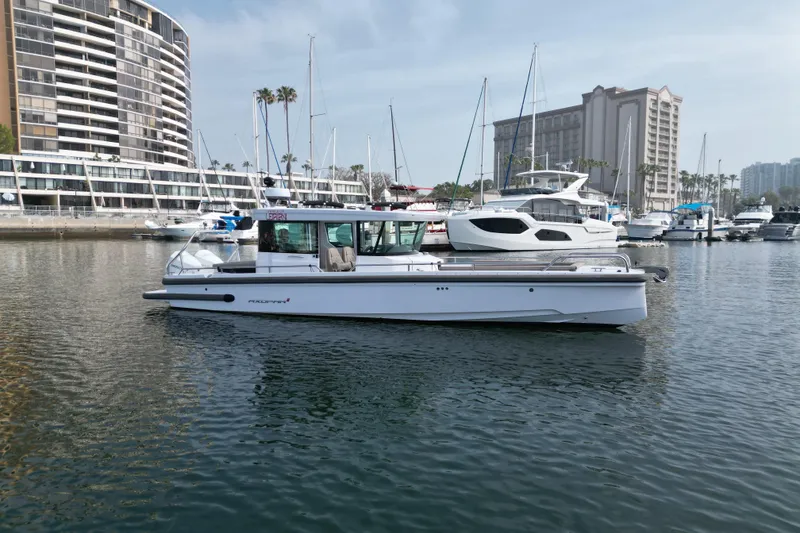 Slide: The Image of 2023 Axopar 28 Cabin boat docked in a marina with modern buildings in the background. - 6