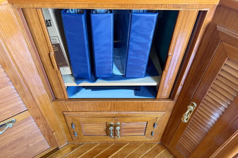 Slide: The Image of Wooden cabinet with blue binders inside, aboard a 1987 PT Sundeck boat. - 26