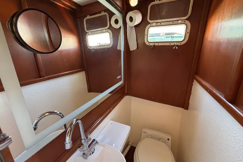 Slide: The Image of Compact bathroom in a 1974 Skookum 34 boat, featuring wood paneling and nautical windows. - 24