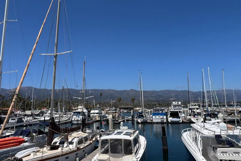 Slide: The Image of Boats docked at a marina with mountains in the background under a clear blue sky. - 7