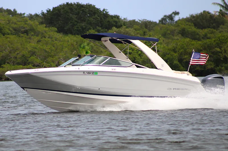 The Image of 2021 Regal 26 OBX boat cruising on water with American flag, lush greenery background. - 0