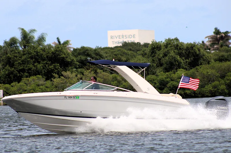 Slide: The Image of 2021 Regal 26 OBX boat cruising on water with American flag, lush greenery background. - 45