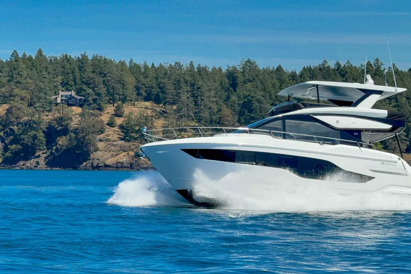 The Image of 2027 Cruisers Yachts 50 Fly navigating scenic waters near a forested shoreline. - 0