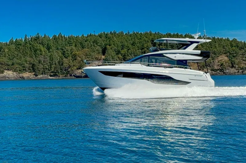 Slide: The Image of 2027 Cruisers Yachts 50 Fly cruising on a serene lake with forested shoreline. - 2