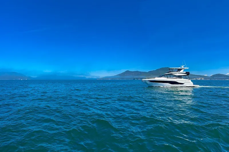 Slide: The Image of 2027 Cruisers Yachts 50 Fly cruising on a clear blue ocean with scenic mountain backdrop. - 5