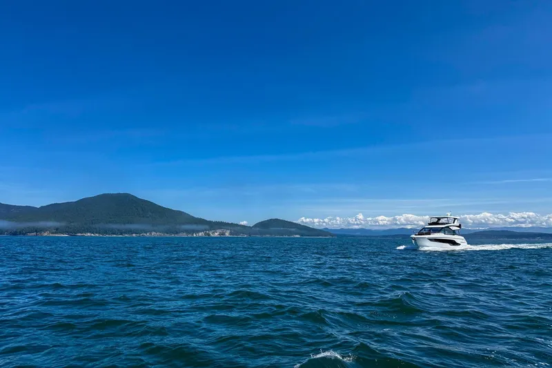 Slide: The Image of 2027 Cruisers Yachts 50 Fly cruising on a clear blue sea with scenic mountain backdrop. - 6