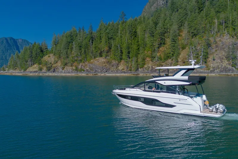 Slide: The Image of 2027 Cruisers Yachts 50 Fly navigating scenic waters with forested mountains in the background. - 7