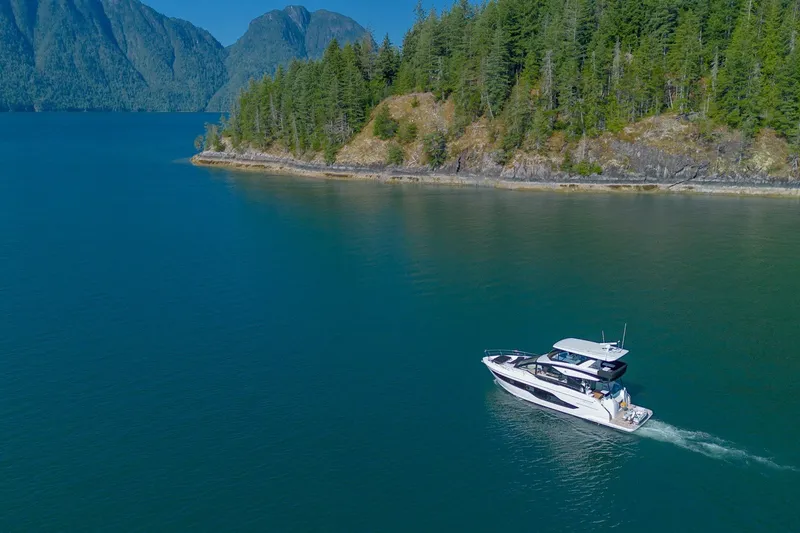 Slide: The Image of 2027 Cruisers Yachts 50 Fly navigating scenic coastal waters with lush forest backdrop. - 8