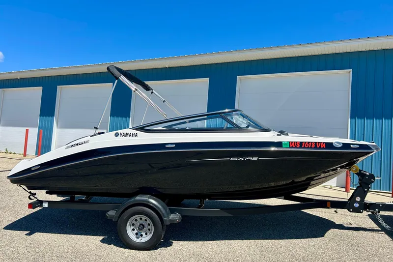 Slide: The Image of 2024 Yamaha Boats SX195 on trailer, parked outside blue building under clear sky. - 11