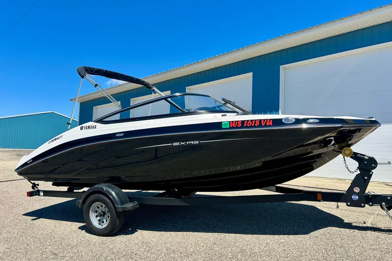Slide: The Image of 2024 Yamaha Boats SX195 on trailer, parked outside blue building under clear sky. - 9