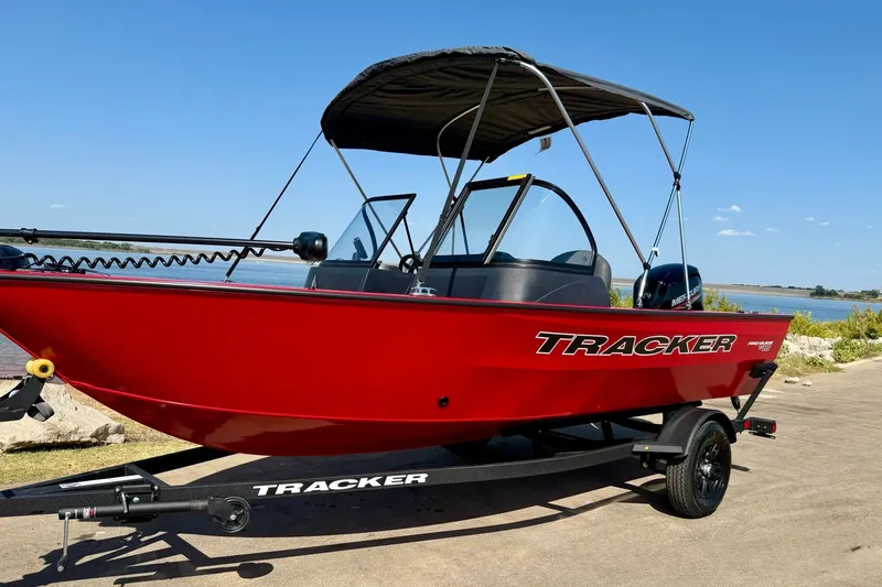 Slide: The Image of 2026 Tracker Pro Guide V-16 WT boat in vibrant red on a trailer by the water. - 13