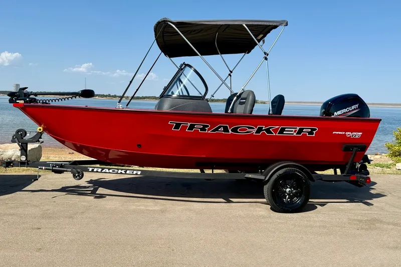 Slide: The Image of 2026 Tracker Pro Guide V-16 WT boat with canopy, parked by a serene lake. - 14
