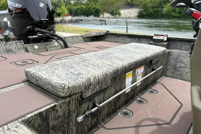 Slide: The Image of 2026 Tracker Grizzly 2072 CC boat interior with camo seating and Mercury engine by a lake. - 17