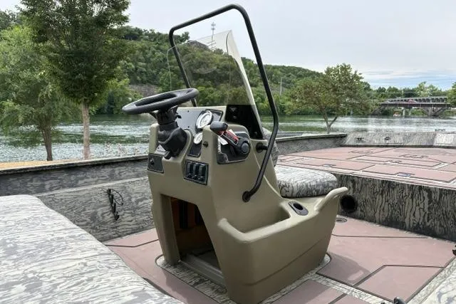 Slide: The Image of 2026 Tracker Grizzly 2072 CC boat interior with steering console, near scenic river and trees. - 19
