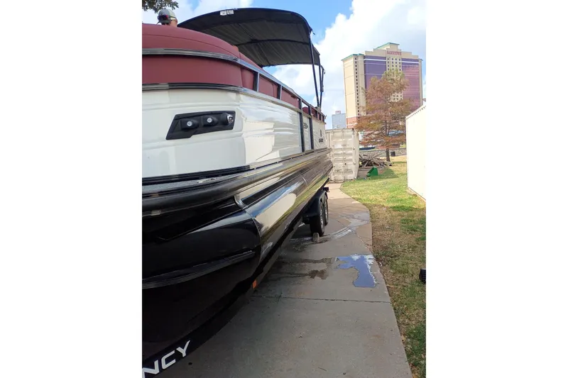 Slide: The Image of 2026 Regency 250 DL3 pontoon boat parked on a driveway near buildings. - 16