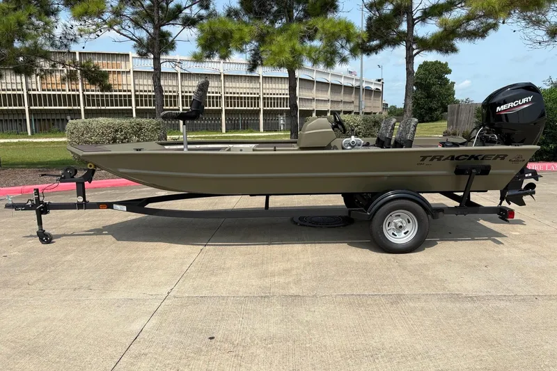The Image of 2026 Tracker Grizzly 1754 SC boat on trailer, parked outdoors with trees in background. - 0