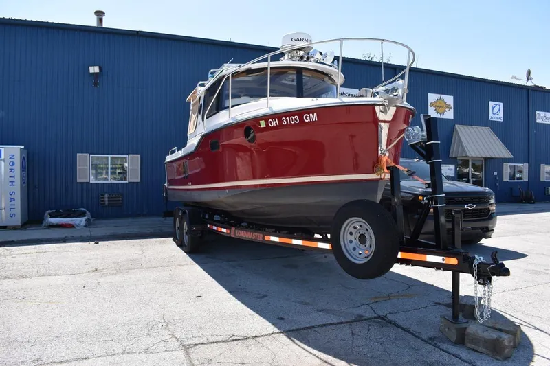The Image of 2024 Ranger Tugs R-25 boat on trailer outside a blue industrial building. - 1