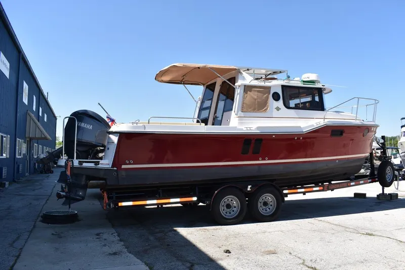 Slide: The Image of 2024 Ranger Tugs R-25 boat on trailer, red hull, parked outdoors. - 29
