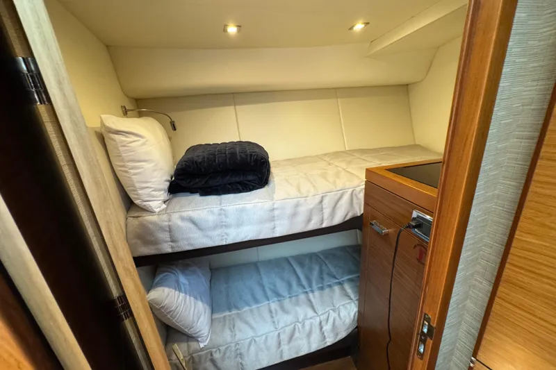 Slide: The Image of Bunk beds in 2017 Tiara Yachts F53 Flybridge cabin, featuring cozy bedding and wooden cabinetry. - 52