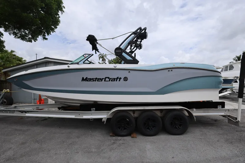 Slide: The Image of 2023 MasterCraft X24 boat on trailer, side view, parked outdoors. - 2