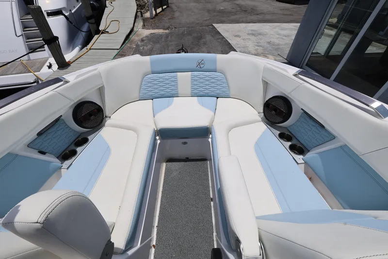 Slide: The Image of 2023 MasterCraft X24 boat interior with white and blue seating, cup holders, and speakers. - 21