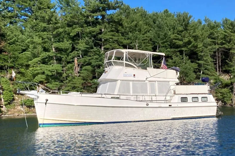 The Image of Grand Banks 42 Motoryacht 1991 anchored on a serene lake with forest backdrop. - 0