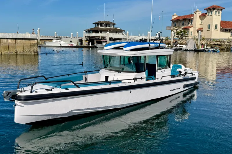 Slide: The Image of 2021 Axopar Brabus 28 Cabin boat docked in a scenic marina setting. - 2