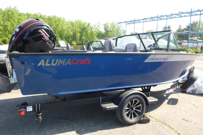 The Image of 2025 Alumacraft Trophy 185X Sport boat on trailer, blue exterior, parked outdoors. - 1