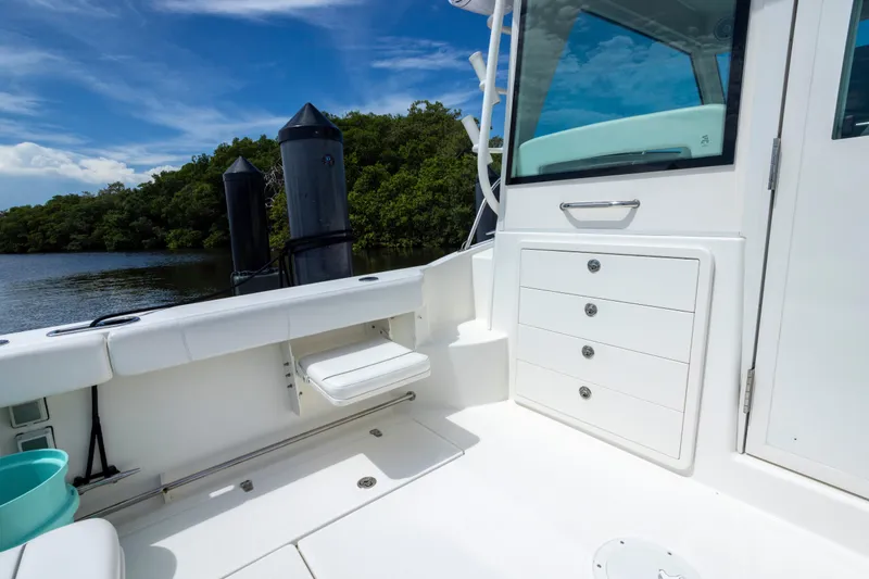 Slide: The Image of 2014 Boston Whaler 315 Conquest boat interior with storage drawers and seating, docked by lush greenery. - 7