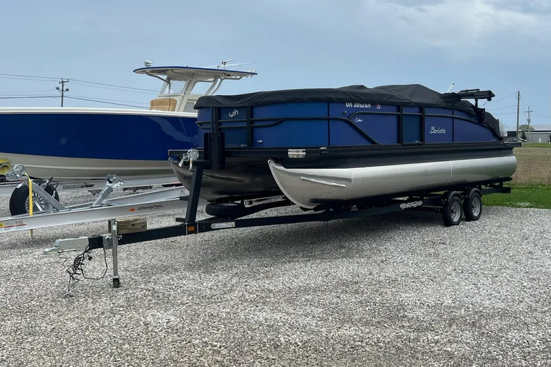 Slide: The Image of 2023 Barletta C22 pontoon boat on trailer, covered and parked on gravel. - 1