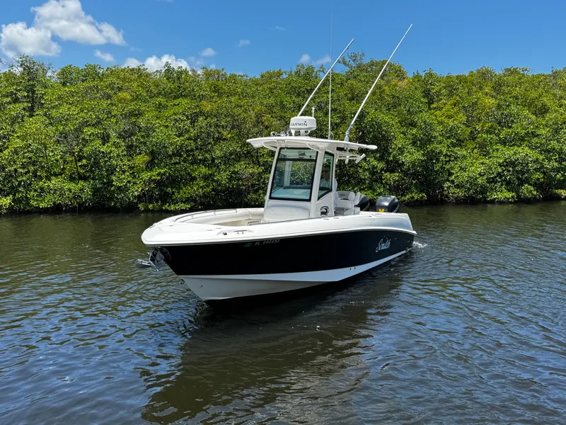 Slide: The Image of 2011 Boston Whaler 280 Outrage on calm water with lush greenery backdrop. - 5