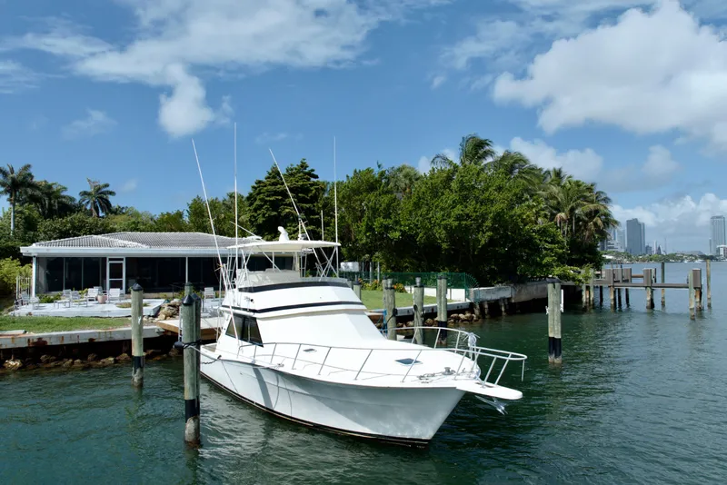 The Image of 1990 Viking 43 Convertible yacht docked by a waterfront house, surrounded by lush greenery. - 0