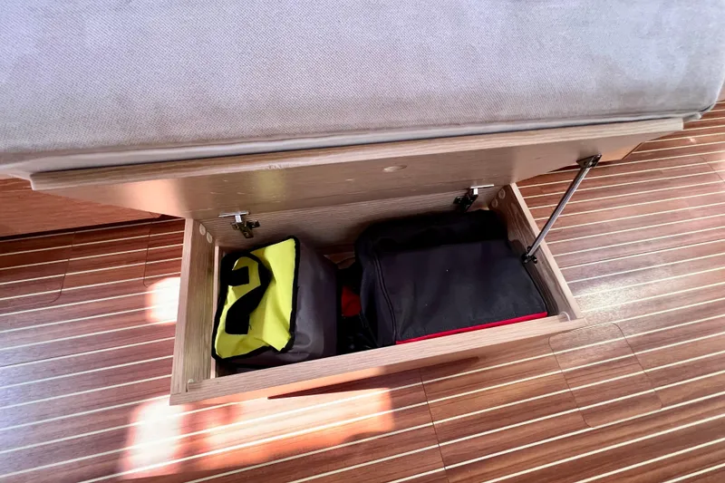Slide: The Image of Storage compartment under seat in 2016 Hanse 455 yacht, containing bags on wooden flooring. - 127