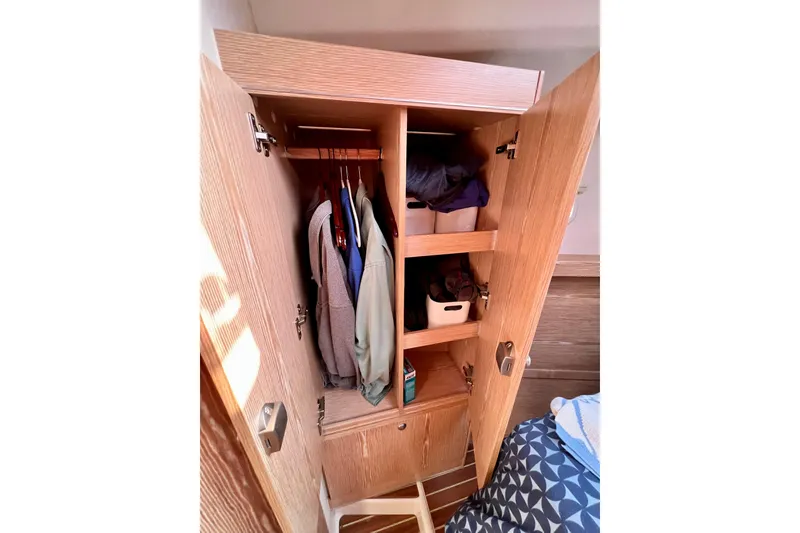 Slide: The Image of Wooden wardrobe interior on a 2016 Hanse 455 yacht, with clothes and storage bins. - 164