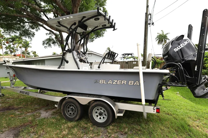 Slide: The Image of 2021 Blazer Bay 2400 boat on trailer with Suzuki engine, parked outdoors. - 2