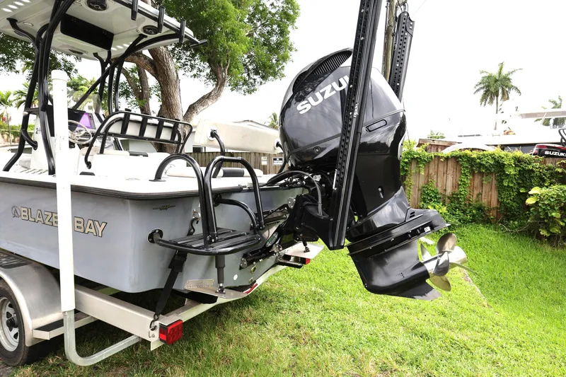 Slide: The Image of 2021 Blazer Bay 2400 boat with Suzuki outboard motor on trailer, parked in a lush yard. - 3
