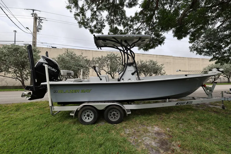 Slide: The Image of 2021 Blazer Bay 2400 boat on trailer, parked on grass under trees. - 7