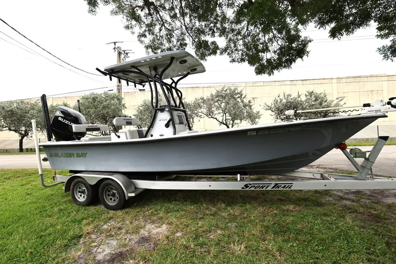 Slide: The Image of 2021 Blazer Bay 2400 boat on trailer, parked outdoors under trees. - 8