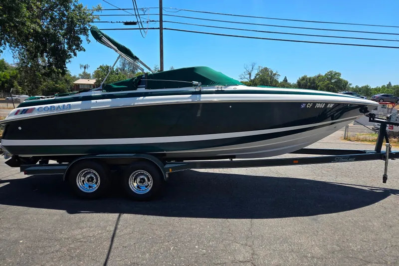 Slide: The Image of 1996 Cobalt 232 boat on trailer, green cover, parked outdoors. - 11