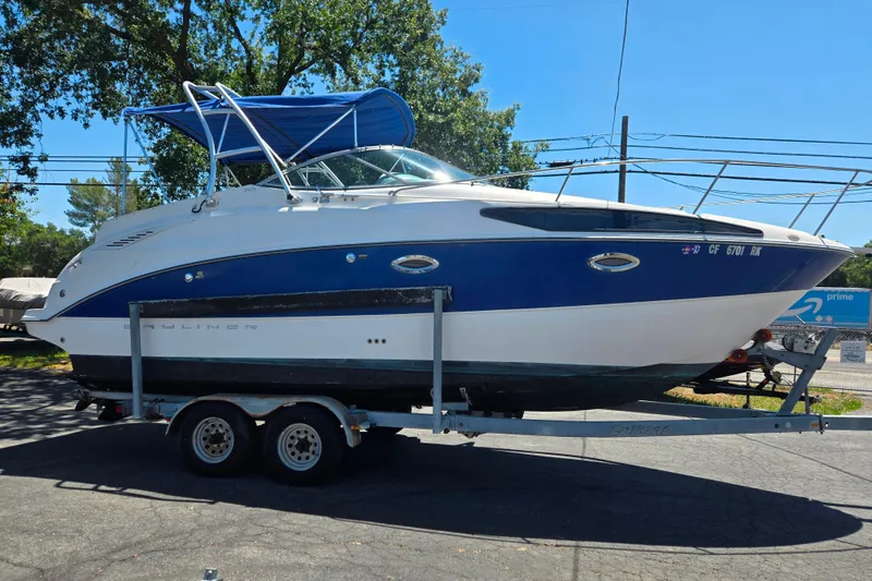 Slide: The Image of 2006 Bayliner 265 boat on trailer with blue canopy, parked outdoors. - 2