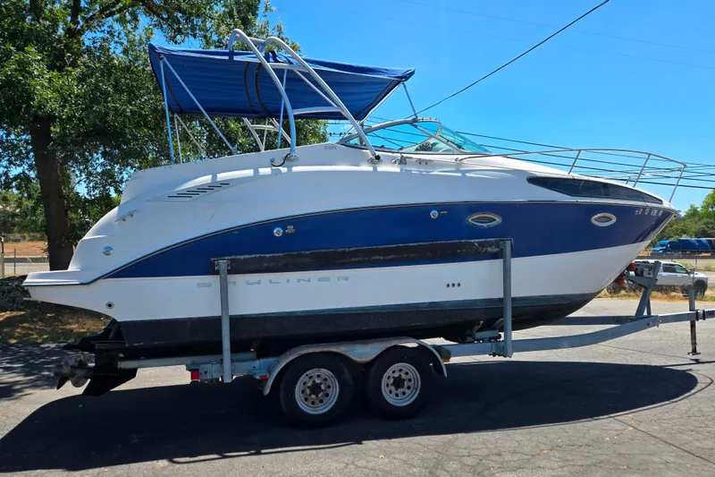 Slide: The Image of 2006 Bayliner 265 boat on trailer, blue and white, parked outdoors under clear sky. - 22