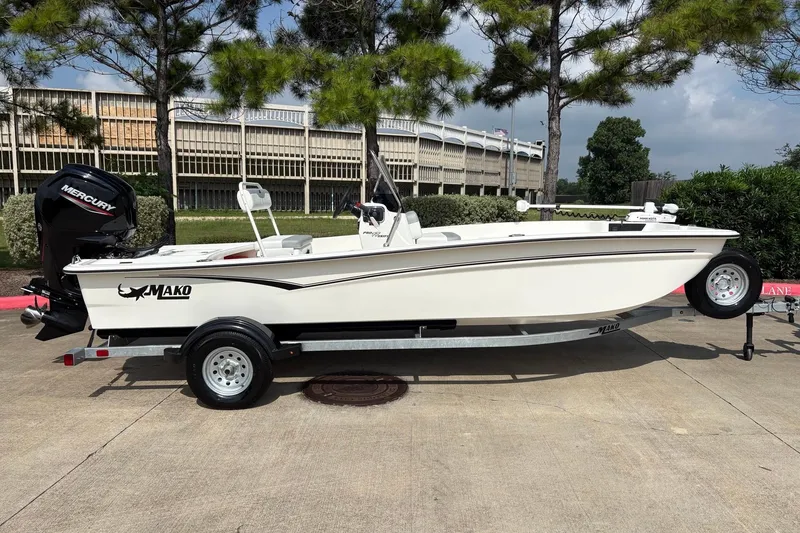 Slide: The Image of 2026 Mako Pro Skiff 17 CC boat on trailer, parked outdoors with trees in background. - 4