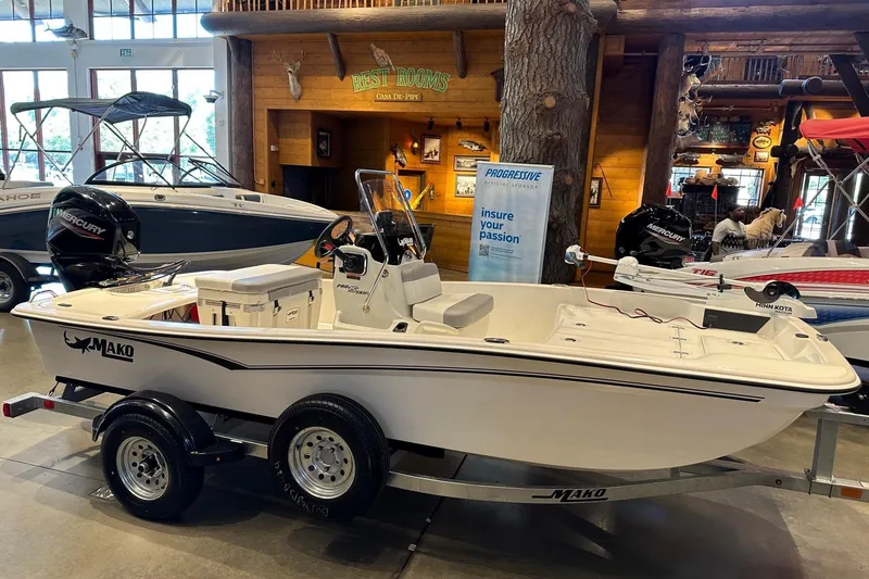 Slide: The Image of 2026 Mako Pro Skiff 15 CC boat displayed indoors, featuring a Mercury engine and trailer. - 2