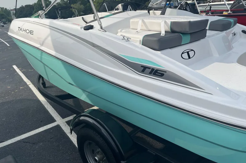 Slide: The Image of 2026 Tahoe T16 boat with teal and white design on a trailer in a parking lot. - 2
