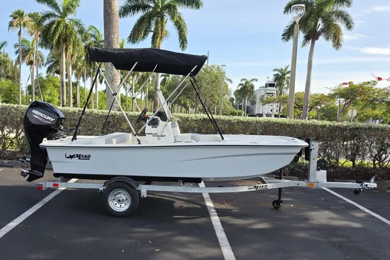 Slide: The Image of 2026 Mako Pro Skiff 13 CC boat on trailer, parked with palm trees in background. - 1
