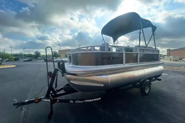 Slide: The Image of 2026 Sun Tracker Bass Buggy 16 XL Select pontoon boat on trailer, parked outdoors. - 2