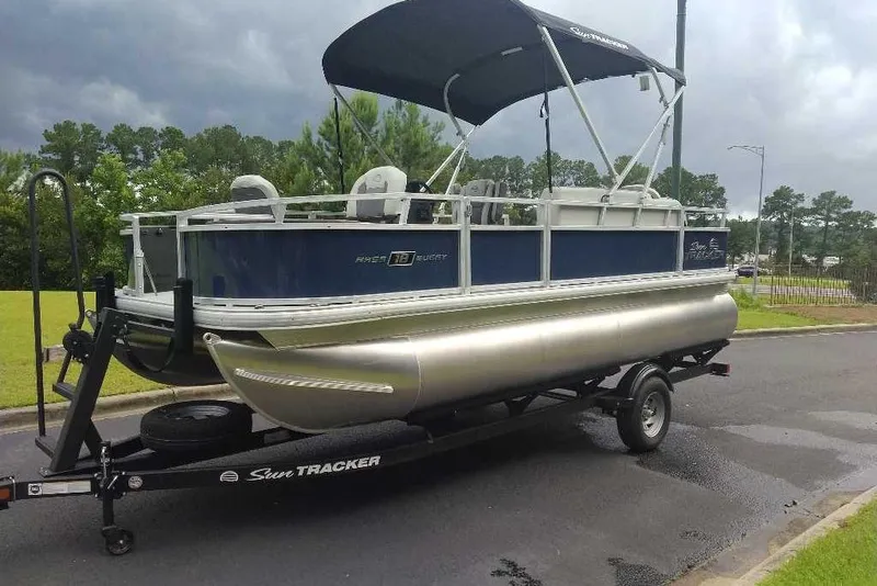 Slide: The Image of 2026 Sun Tracker Bass Buggy 18 DLX pontoon boat on trailer, parked outdoors. - 7