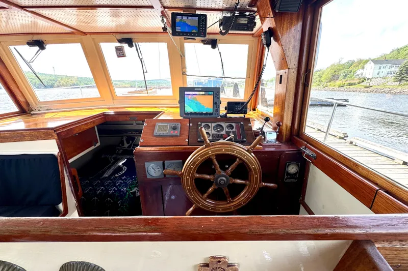 Slide: The Image of 1976 Downeast Flybridge Cruiser helm with wooden wheel and navigation equipment, docked by scenic waters. - 11
