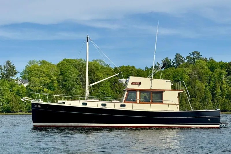 Slide: The Image of 1976 Downeast Flybridge Cruiser on calm water, surrounded by lush green trees. - 3